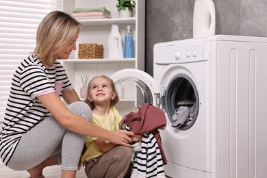 Photo of Housewife and her daughter doing laundry together indoors