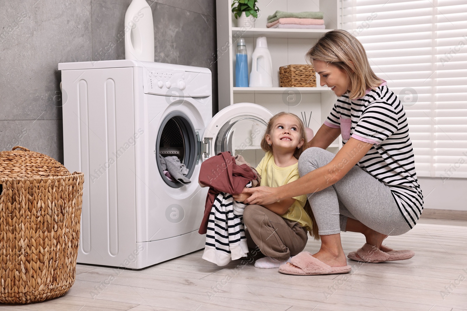 Photo of Housewife and her daughter doing laundry together indoors