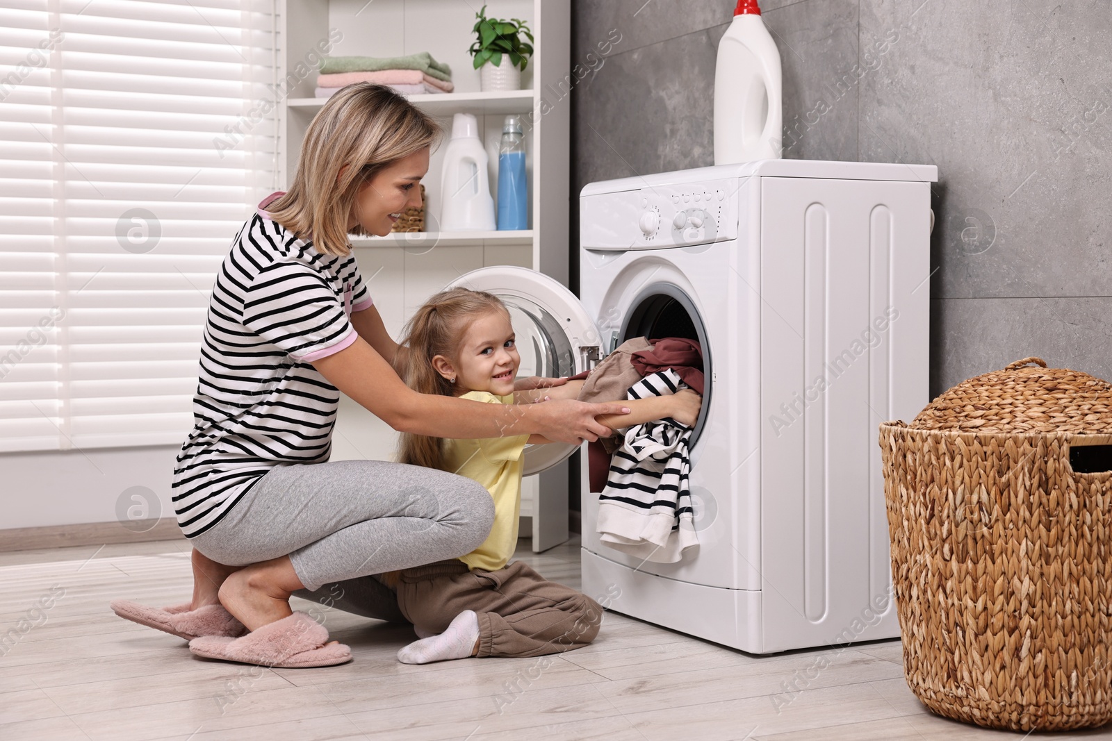 Photo of Housewife and her daughter doing laundry together indoors