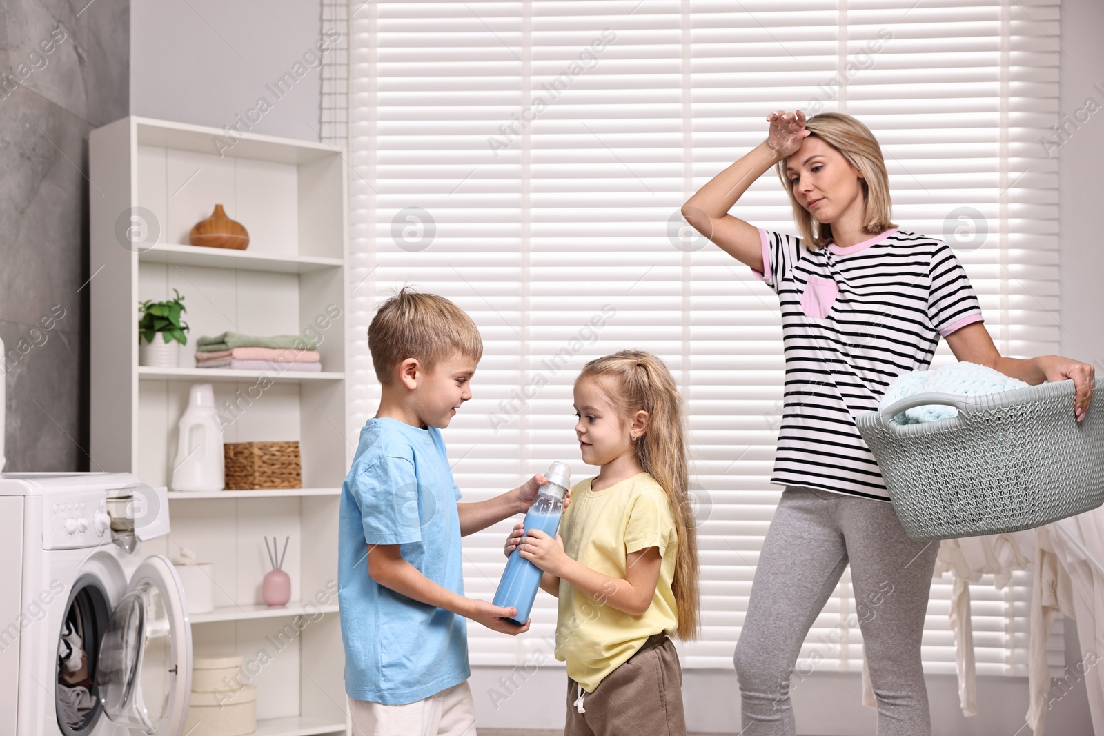 Photo of Tired housewife doing laundry while her kids playing indoors