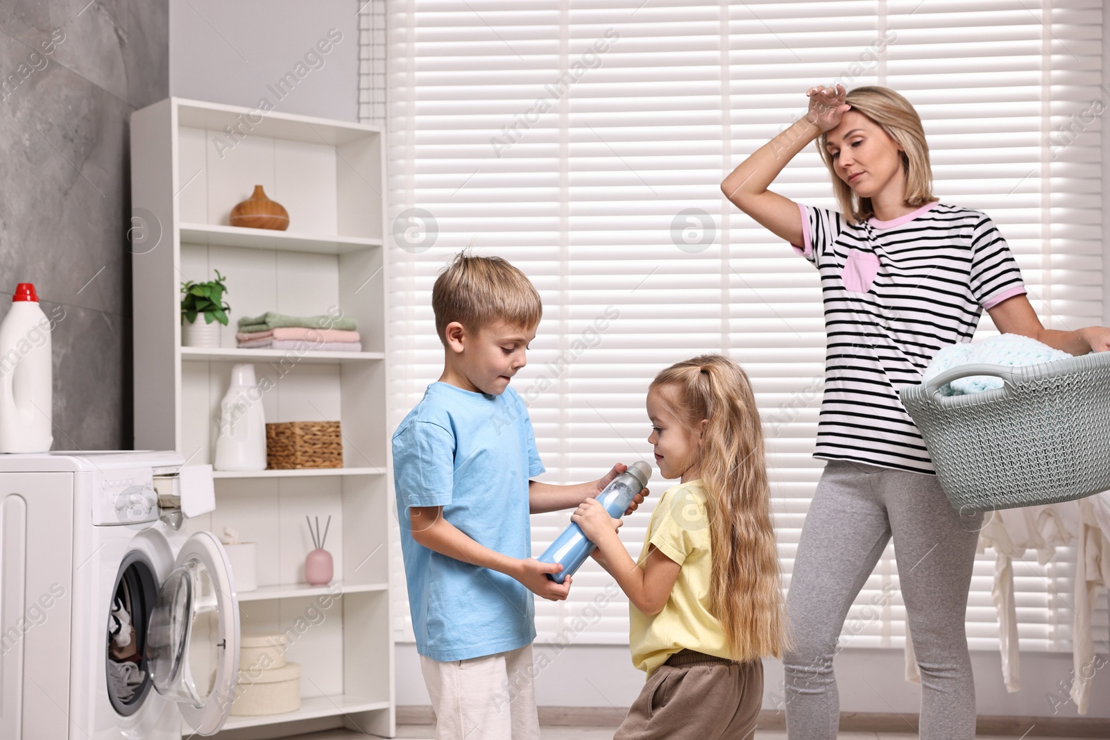 Photo of Tired housewife doing laundry while her kids playing indoors