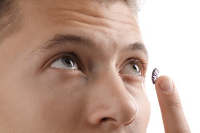 Photo of Man putting color contact lens in his eye on white background, closeup