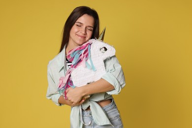 Photo of Woman with unicorn shaped pinata on yellow background