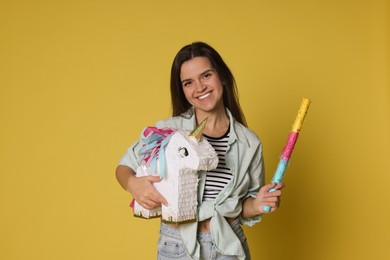 Photo of Happy woman with unicorn shaped pinata and stick on yellow background