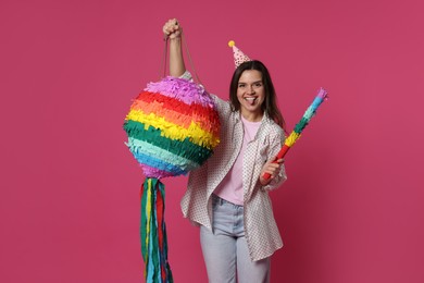 Happy woman with colorful pinata and stick on pink background