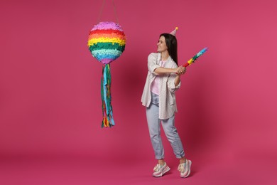 Photo of Happy woman hitting colorful pinata with stick on pink background