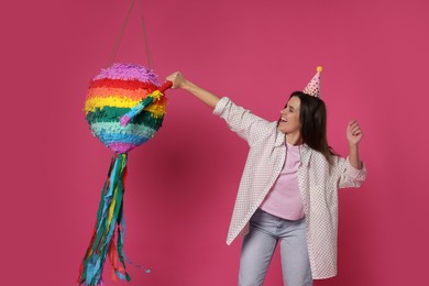 Happy woman hitting colorful pinata with stick on pink background