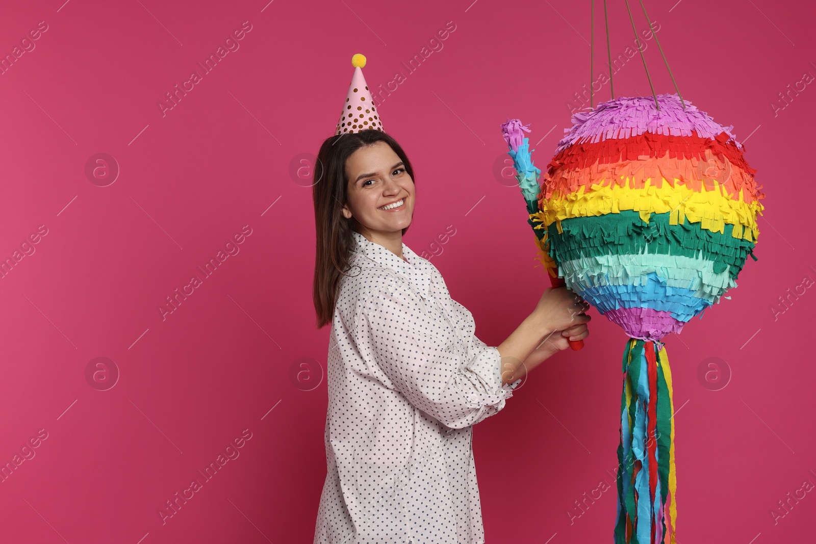 Photo of Happy woman with colorful pinata and stick on pink background