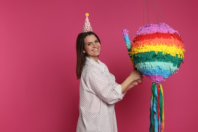 Happy woman with colorful pinata and stick on pink background