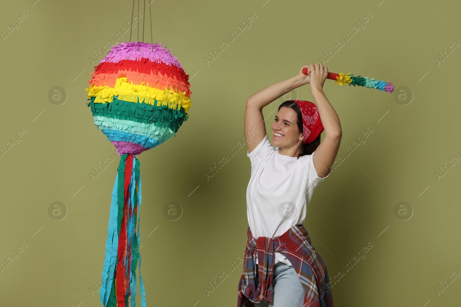 Photo of Happy woman hitting colorful pinata with stick on green background