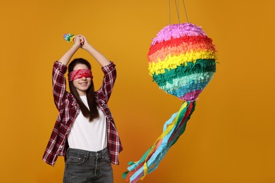 Photo of Woman with tied eyes breaking pinata on orange background