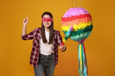 Photo of Woman with tied eyes breaking pinata on orange background