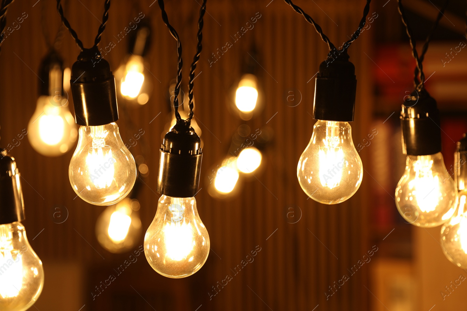 Photo of Glowing light bulbs hanging indoors, closeup view