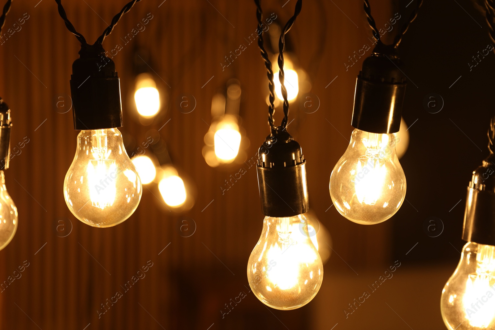 Photo of Glowing light bulbs hanging indoors, closeup view