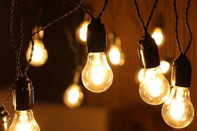 Photo of Glowing light bulbs hanging indoors, closeup view