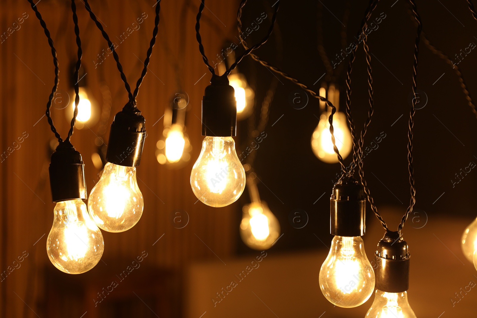 Photo of Glowing light bulbs hanging indoors, closeup view