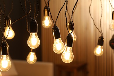 Photo of Glowing light bulbs hanging indoors, closeup view