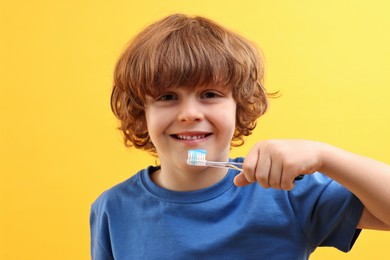 Photo of Cute boy with toothbrush and paste on yellow background