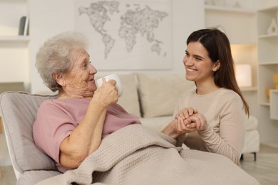 Photo of Grandmother with hot drink and her granddaughter at home. Elderly care