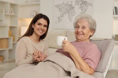 Grandmother with hot drink and her granddaughter at home. Elderly care