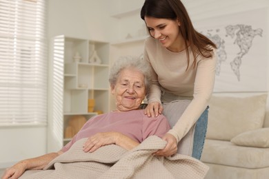 Granddaughter covering her grandmother with blanket at home. Elderly care