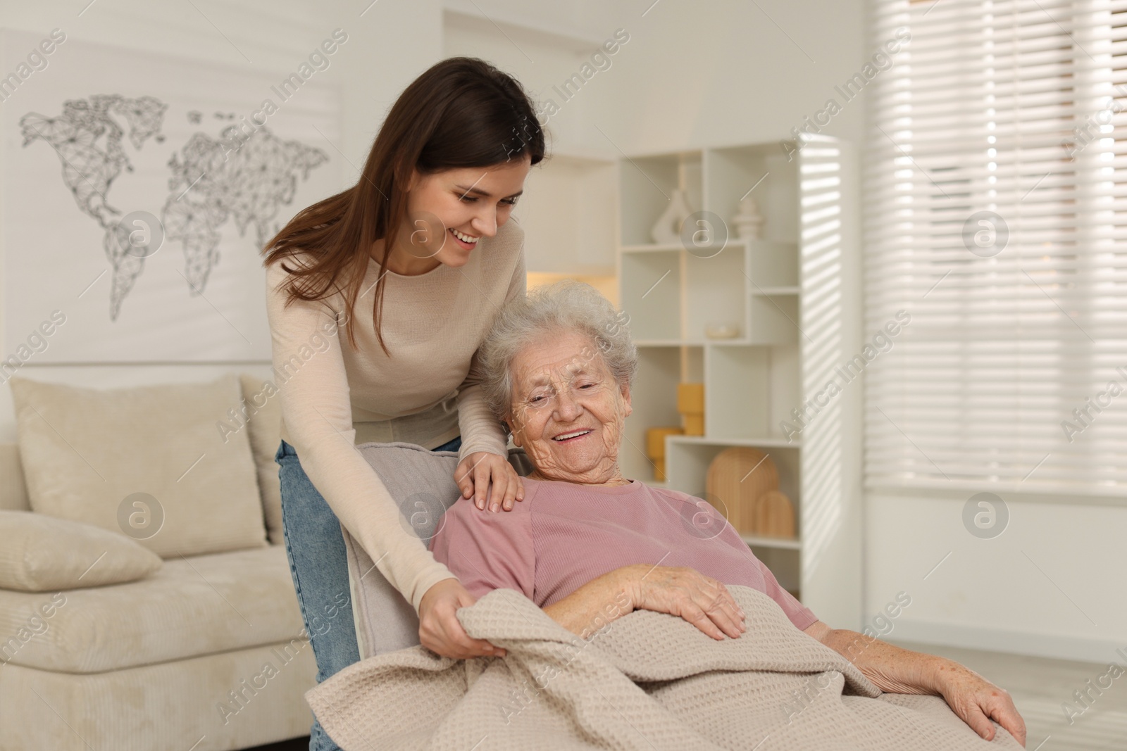 Photo of Granddaughter covering her grandmother with blanket at home. Elderly care