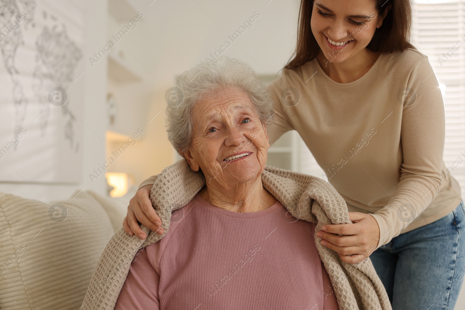 Photo of Granddaughter covering her grandmother with blanket at home. Elderly care