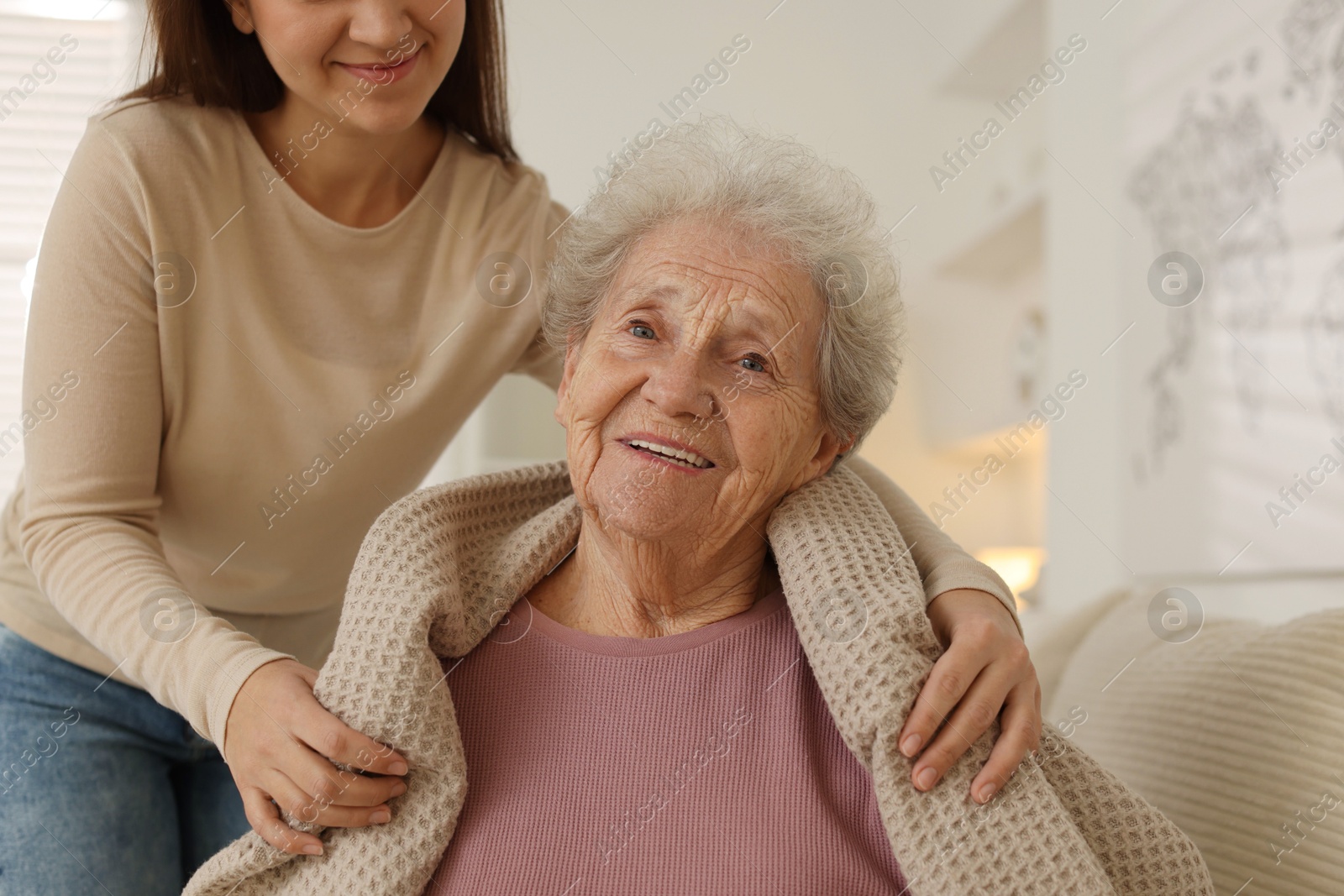 Photo of Granddaughter covering her grandmother with blanket at home, closeup. Elderly care