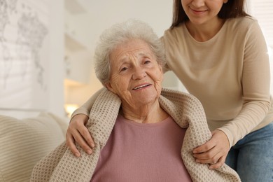 Photo of Granddaughter covering her grandmother with blanket at home, closeup. Elderly care