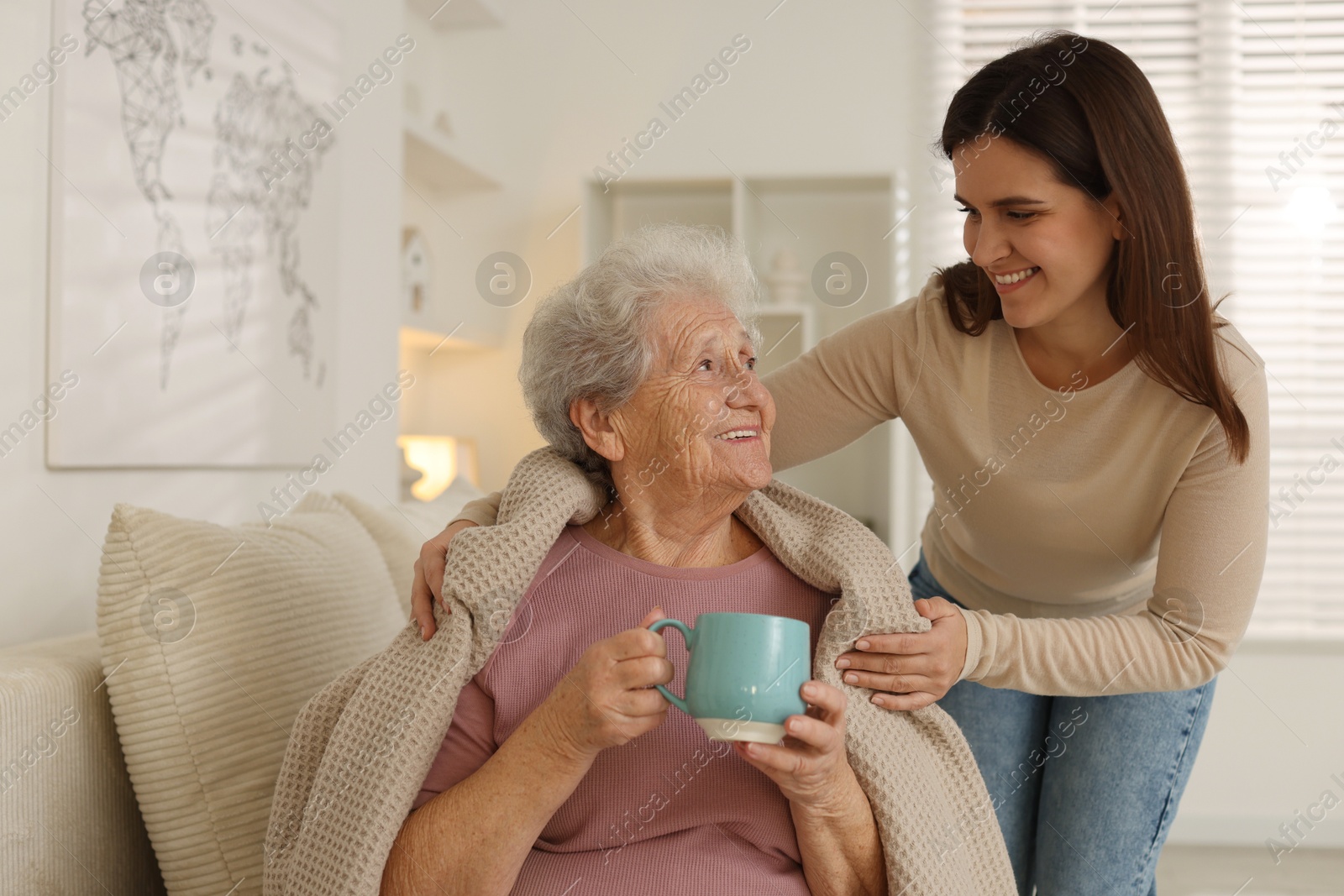 Photo of Granddaughter giving hot drink to her grandmother at home. Elderly care