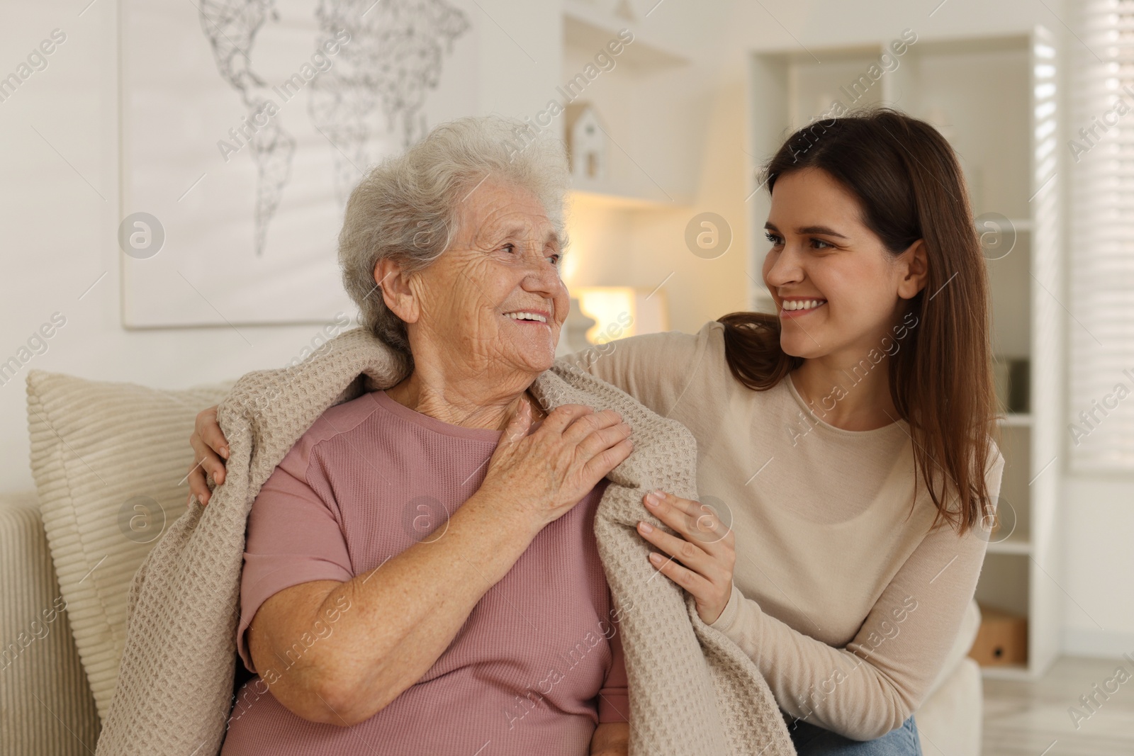 Photo of Granddaughter covering her grandmother with blanket at home. Elderly care