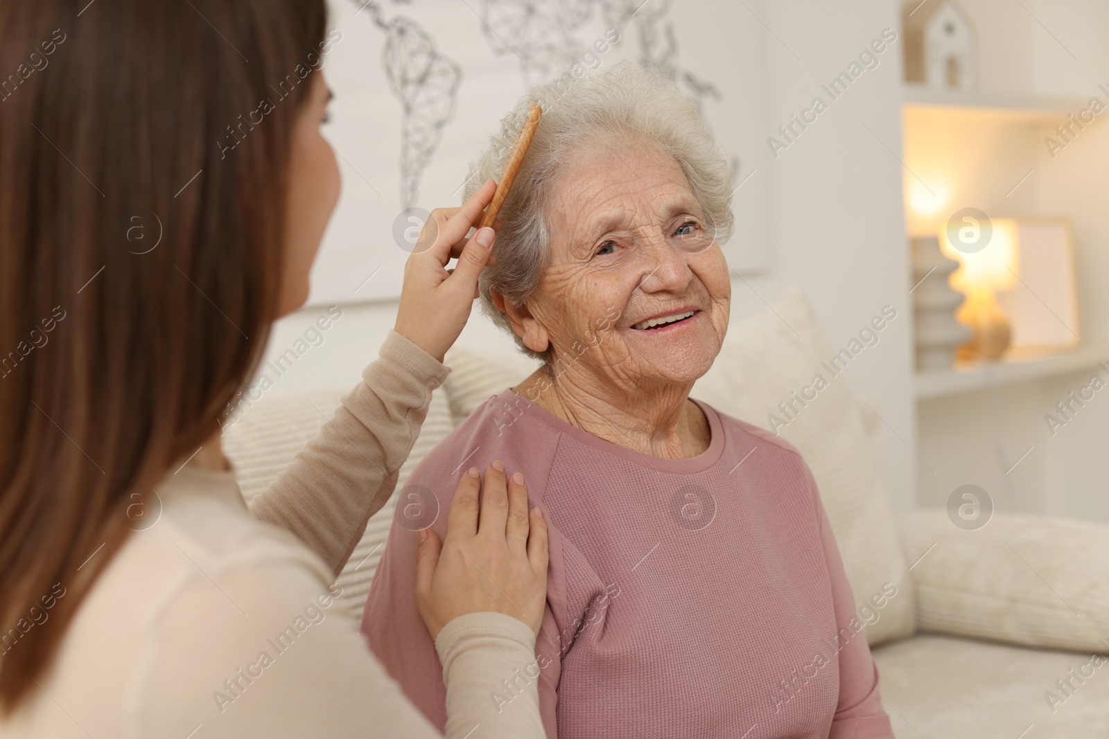 Photo of Granddaughter brushing her grandmother with comb at home, selective focus. Elderly care