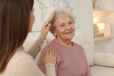 Granddaughter brushing her grandmother with comb at home, selective focus. Elderly care