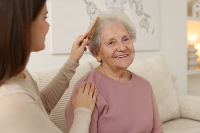 Photo of Granddaughter brushing her grandmother with comb at home, selective focus. Elderly care