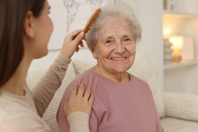 Granddaughter brushing her grandmother with comb at home, selective focus. Elderly care