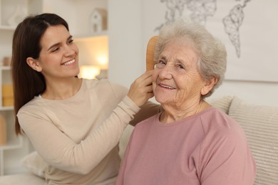 Photo of Granddaughter brushing her grandmother with comb at home. Elderly care