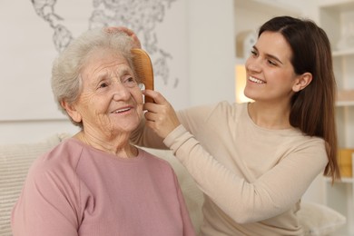 Photo of Granddaughter brushing her grandmother with comb at home. Elderly care