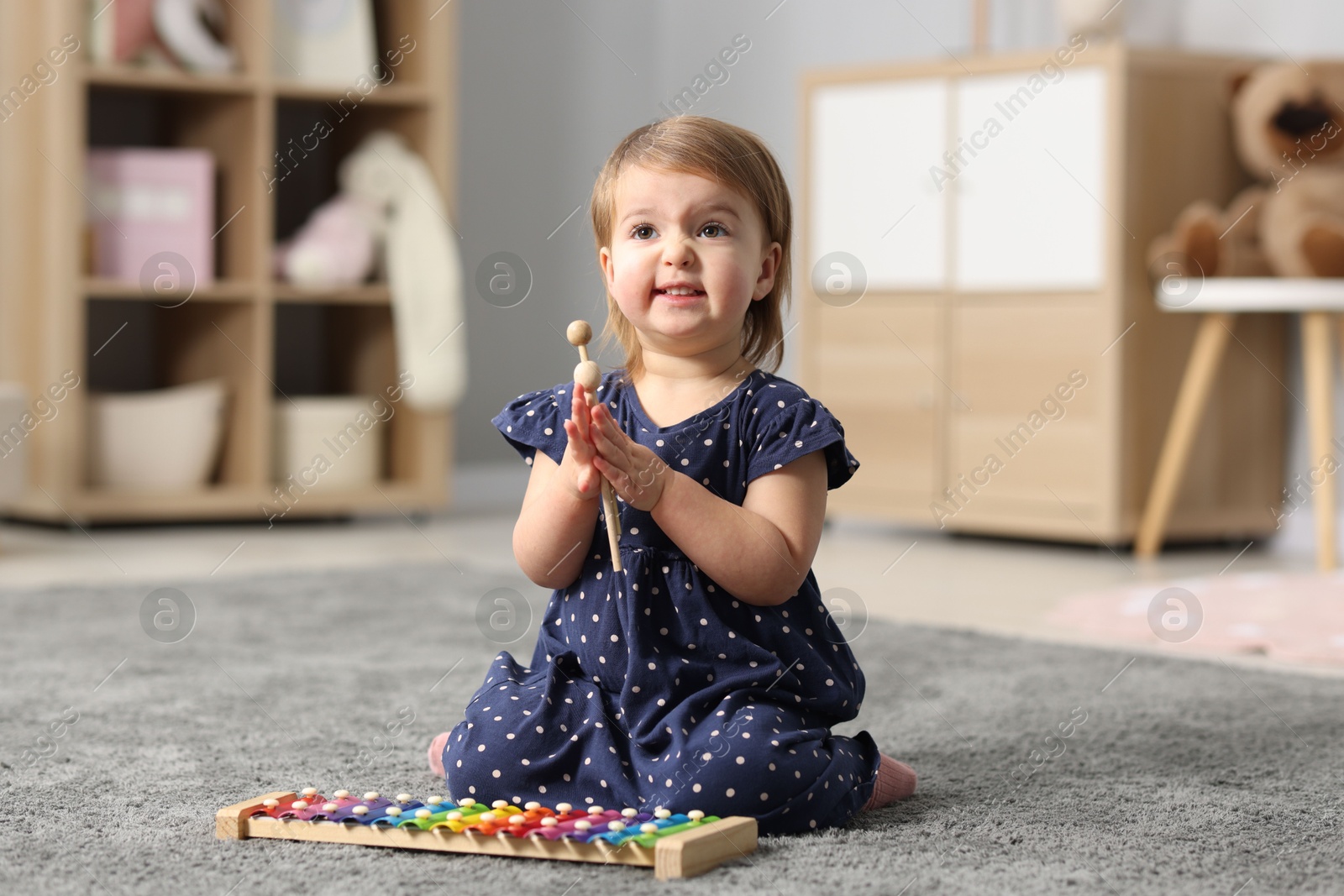 Photo of Cute little girl playing with toy xylophone on floor at home