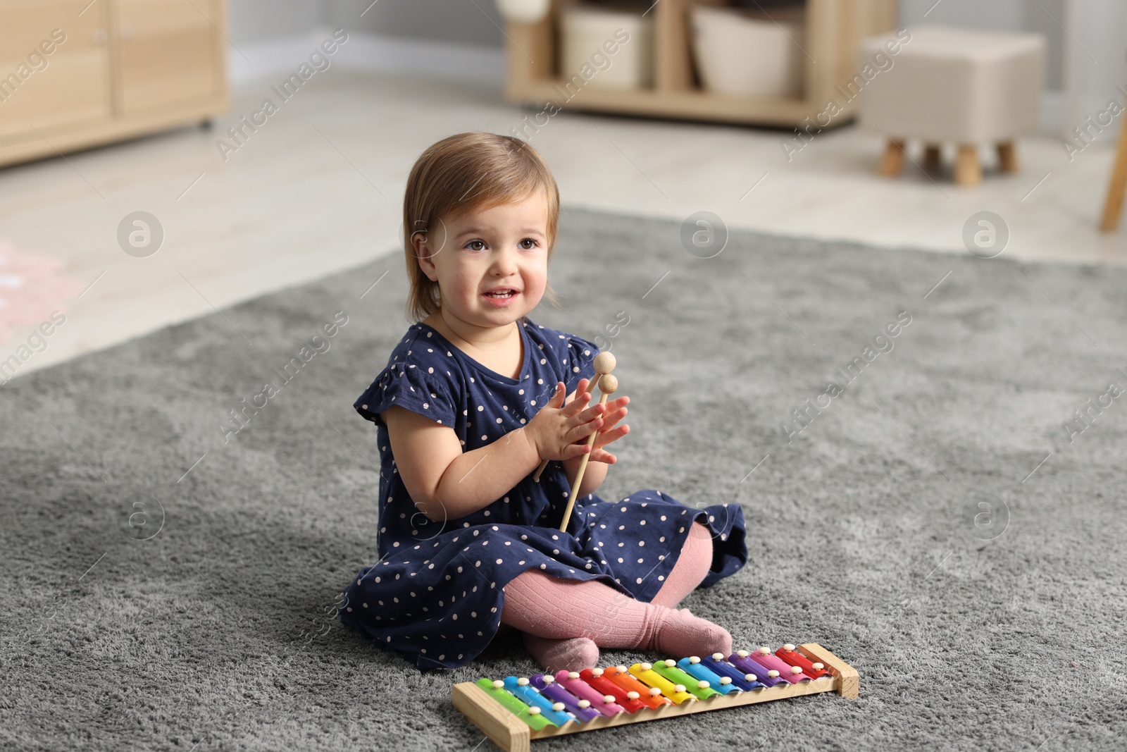 Photo of Cute little girl playing with toy xylophone on floor at home