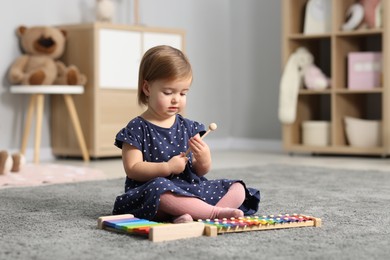 Photo of Cute little girl playing with toy xylophones on floor at home