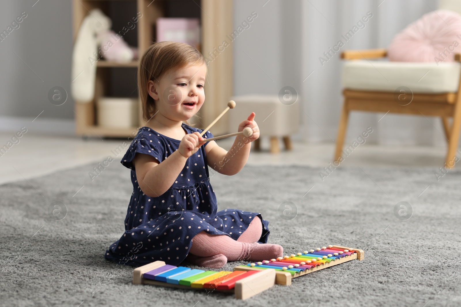 Photo of Cute little girl playing with toy xylophones on floor at home