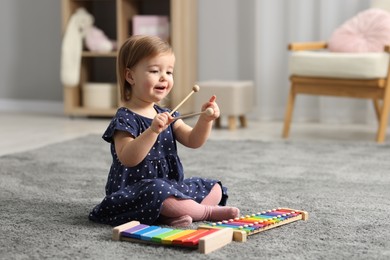 Photo of Cute little girl playing with toy xylophones on floor at home