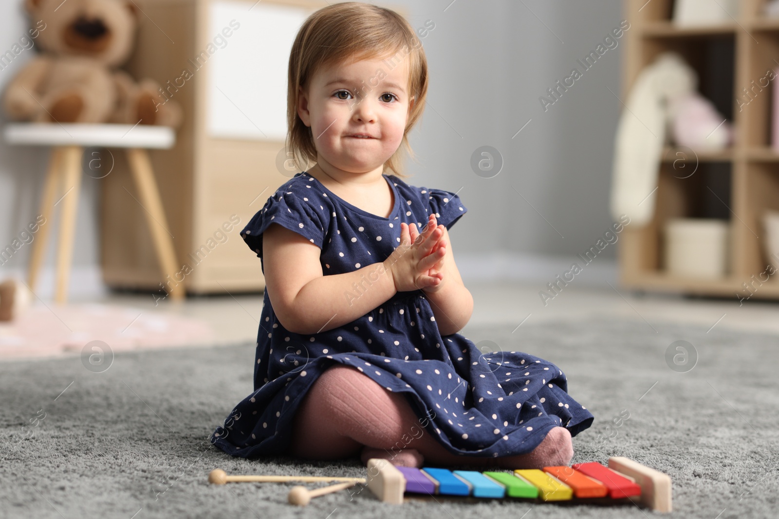 Photo of Cute little girl playing with toy xylophone on floor at home