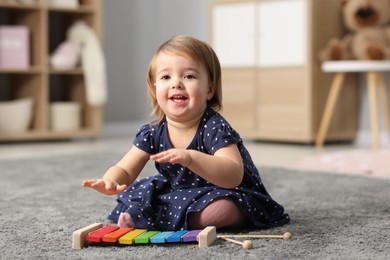 Photo of Cute little girl playing with toy xylophone on floor at home