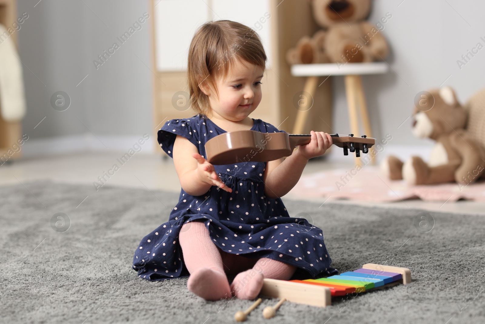 Photo of Cute little girl playing with toy guitar on floor at home