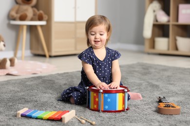 Photo of Cute little girl playing with toy drum on floor at home