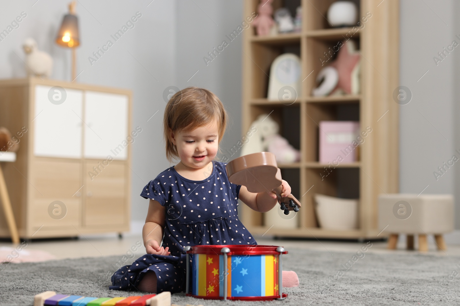 Photo of Cute little girl playing with toy musical instruments on floor at home