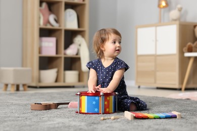 Photo of Cute little girl playing with toy drum on floor at home