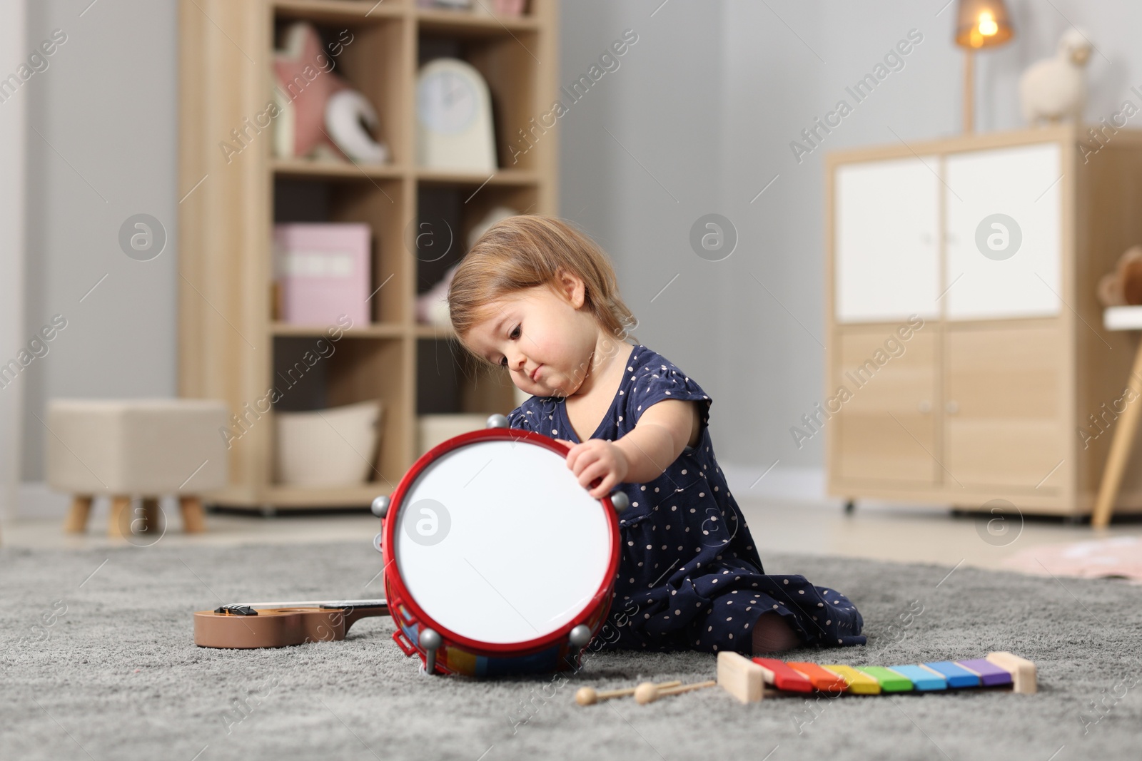 Photo of Cute little girl playing with toy drum on floor at home