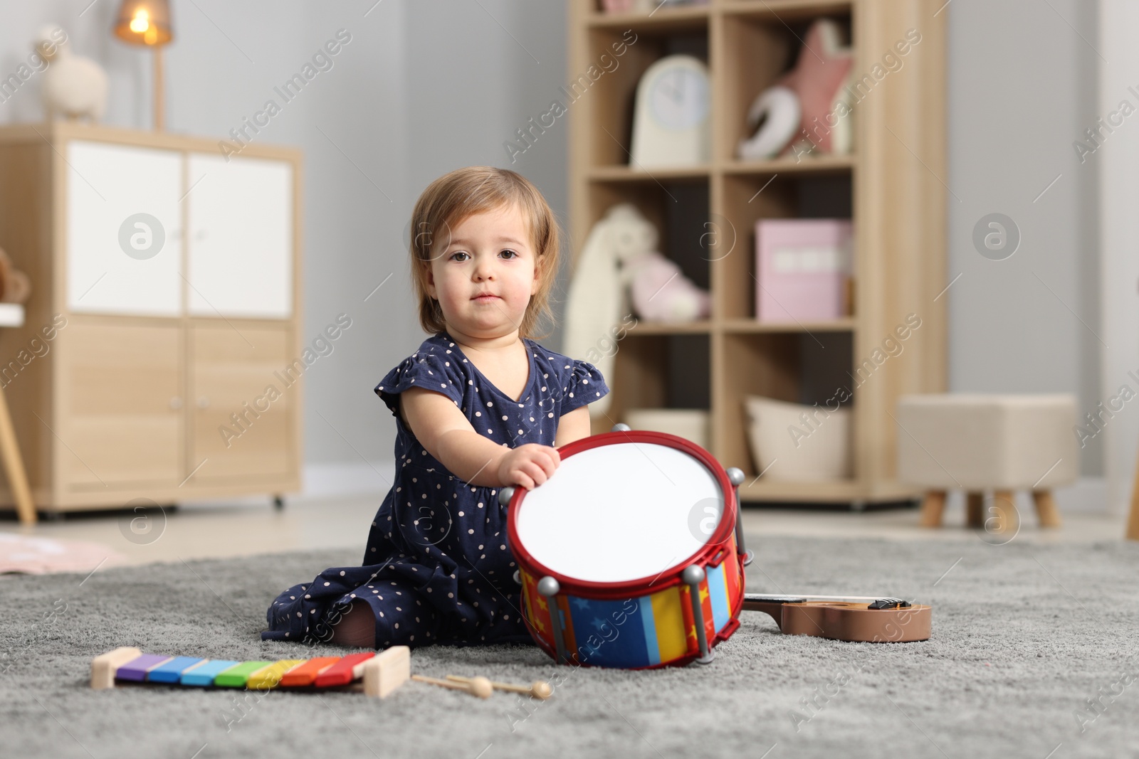 Photo of Cute little girl playing with toy drum on floor at home